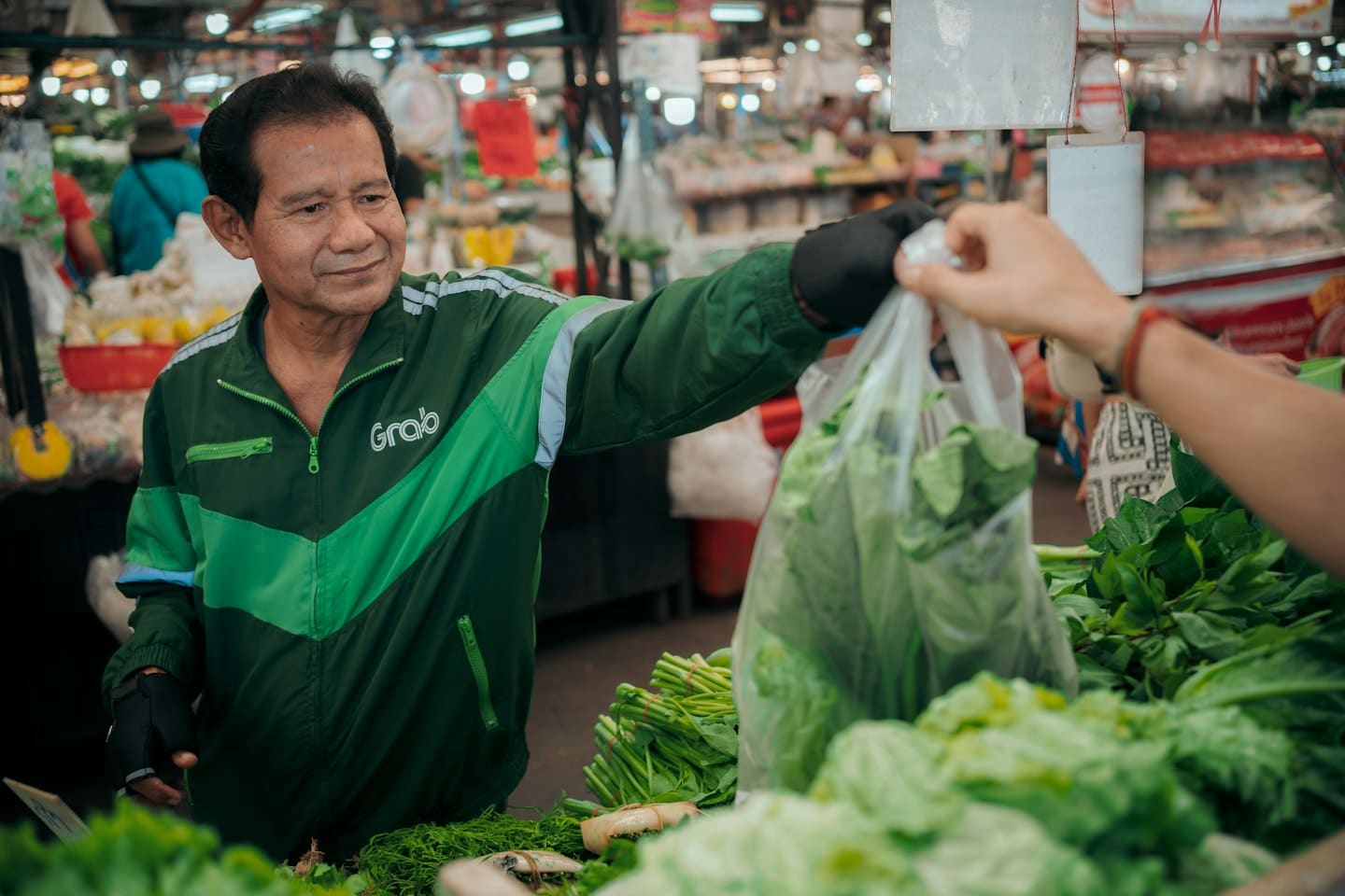 Hombre con chaqueta verde entrega bolsa de verduras a un cliente.