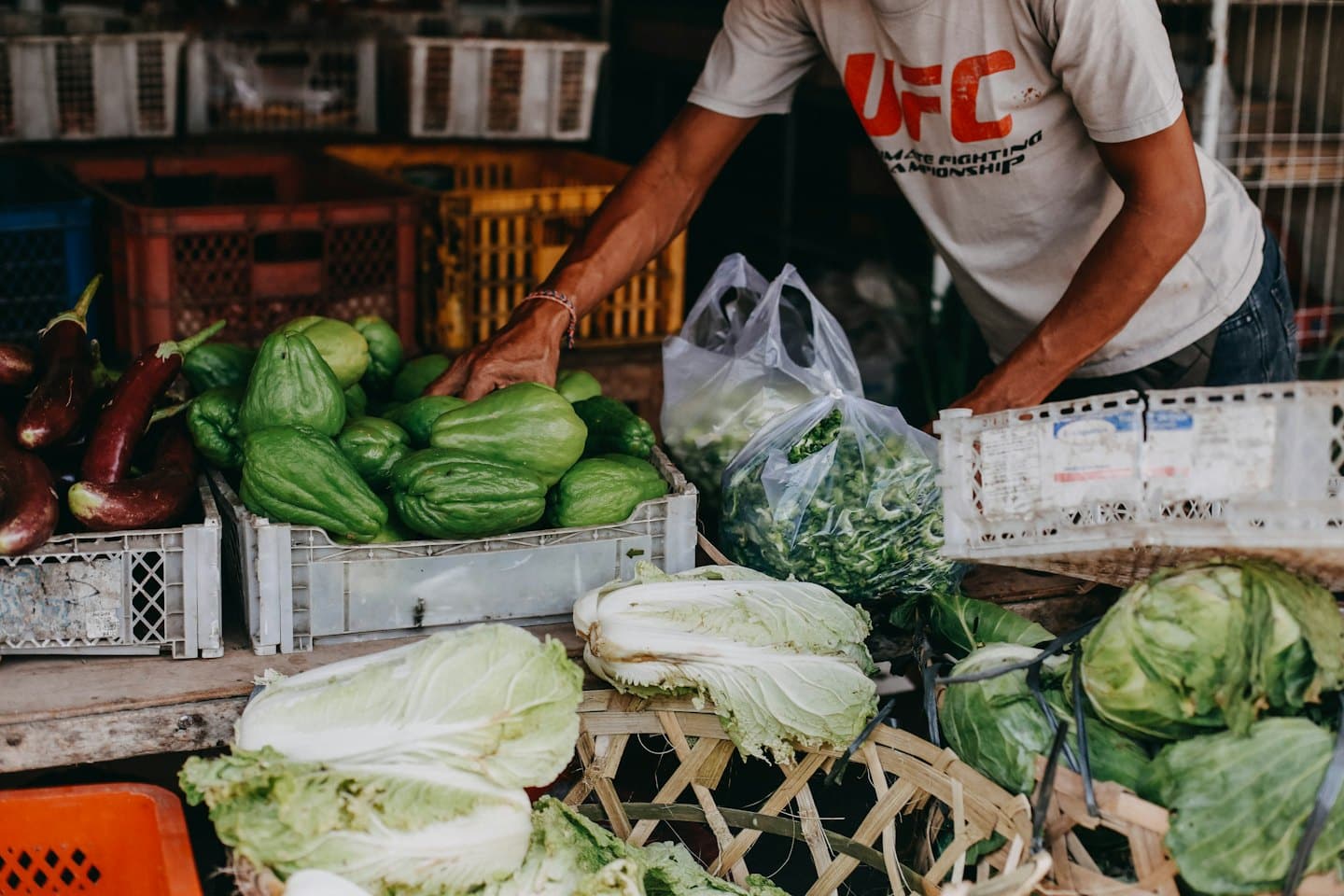 Comerciante eligiendo chayote y berenjena en un puesto de mercado al aire libre.