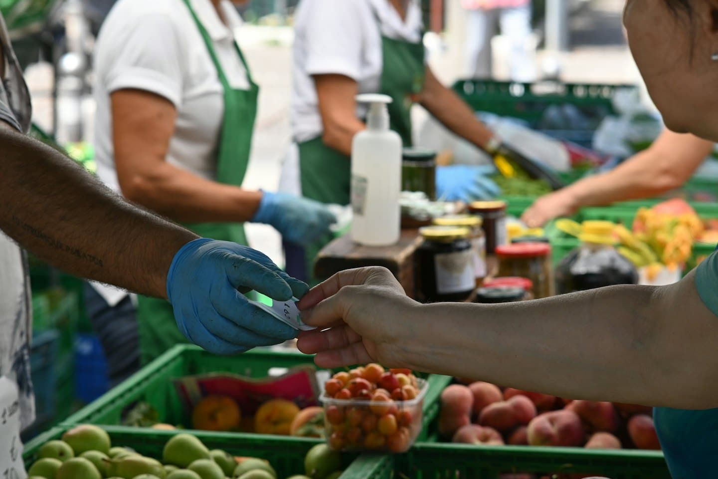 Un vendedor con guantes azules le da un recibo a un cliente en un mercado al aire libre.